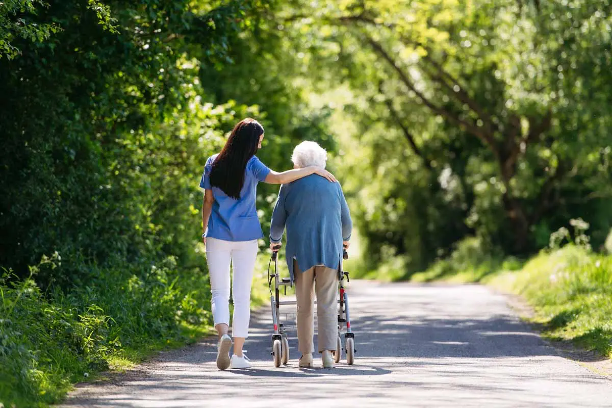 A caregiver walking outdoors supporting an older person