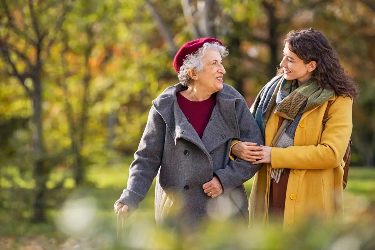 An adult daughter walking arm in arm with her mother outdoors in autumn