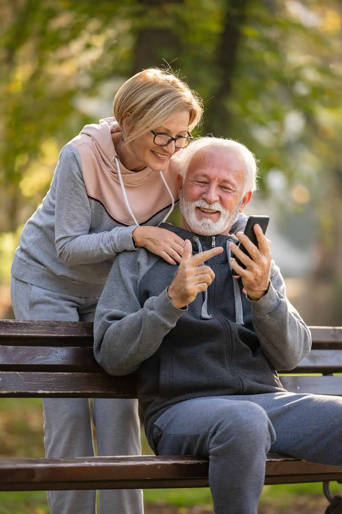 An older couple sitting on a park bench, looking at a phone together